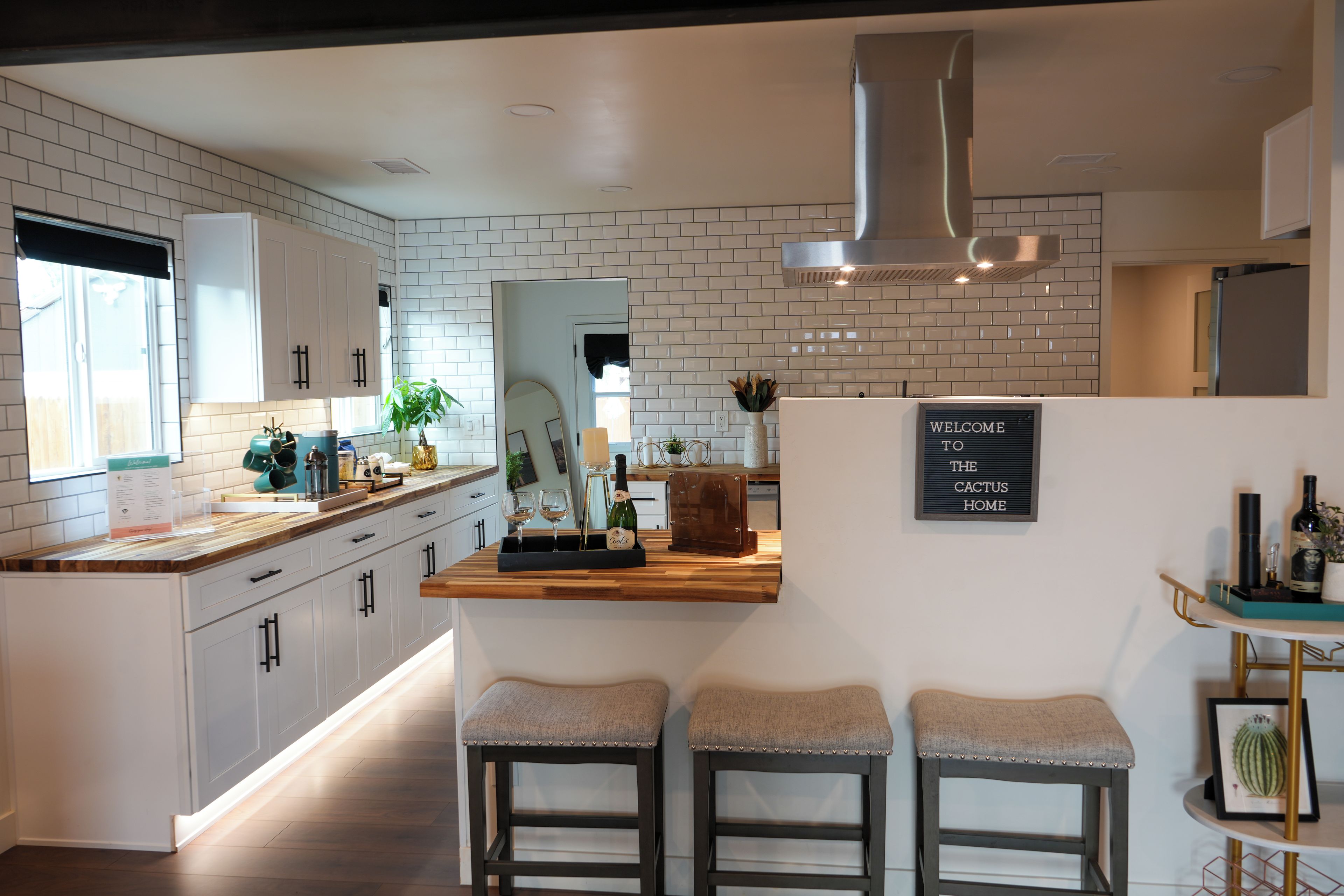 A modern kitchen with white cabinetry, a wooden countertop, and a bar area with stools.