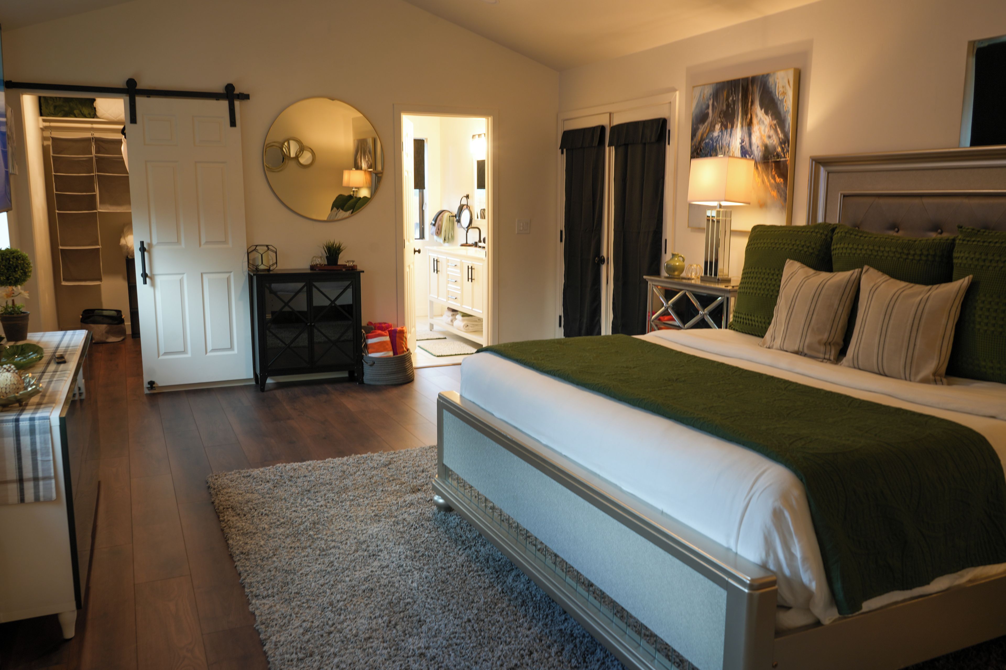A bedroom with a bed, bedside table, lamp, and a view of the bathroom.
