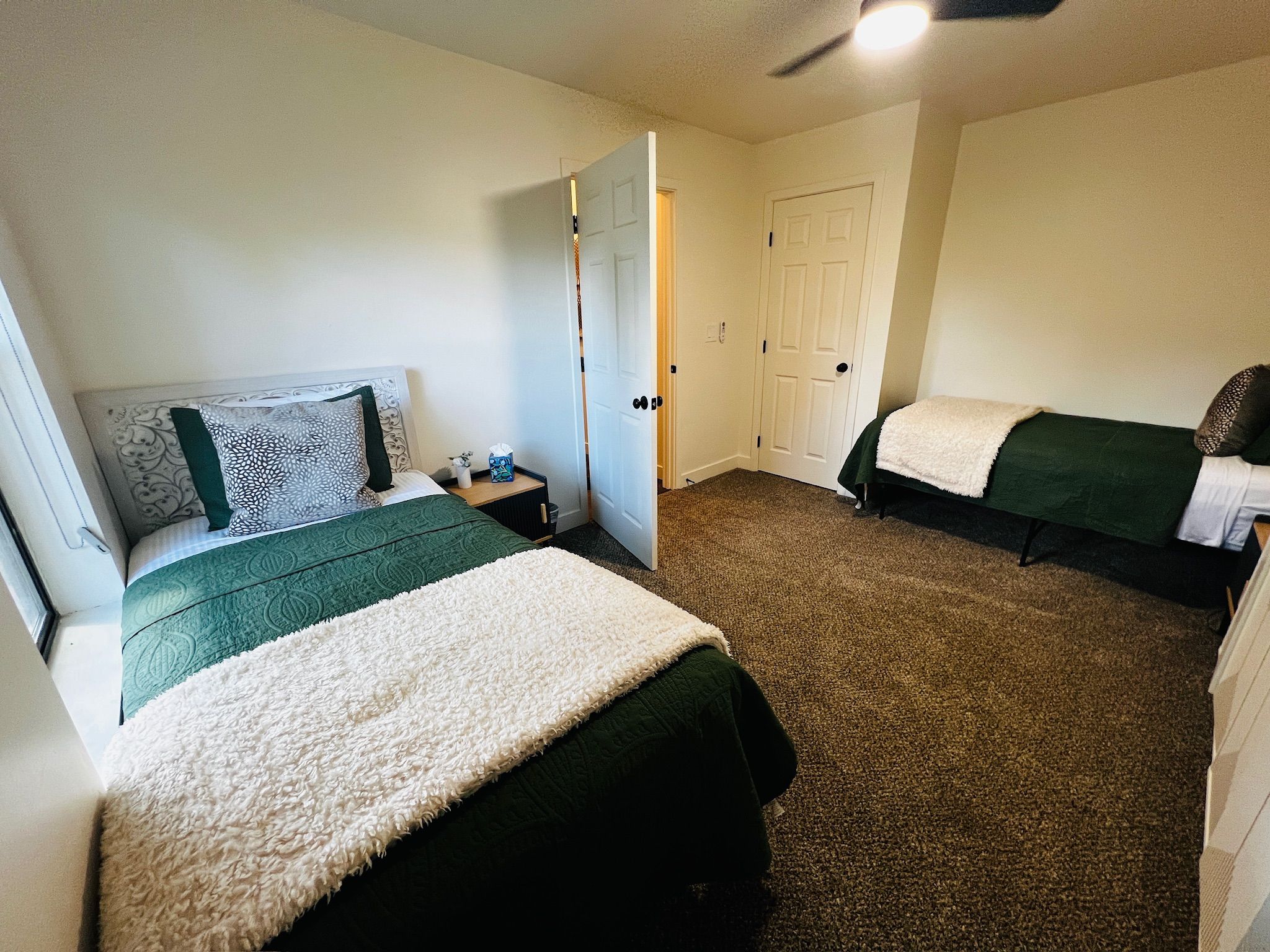 A bedroom with two beds, a nightstand, a door, and a carpeted floor.