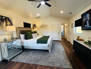 Une chambre à coucher comprenant un lit, des tables de chevet, un ventilateur de plafond, des œuvres d’art et une vue sur une autre pièce.