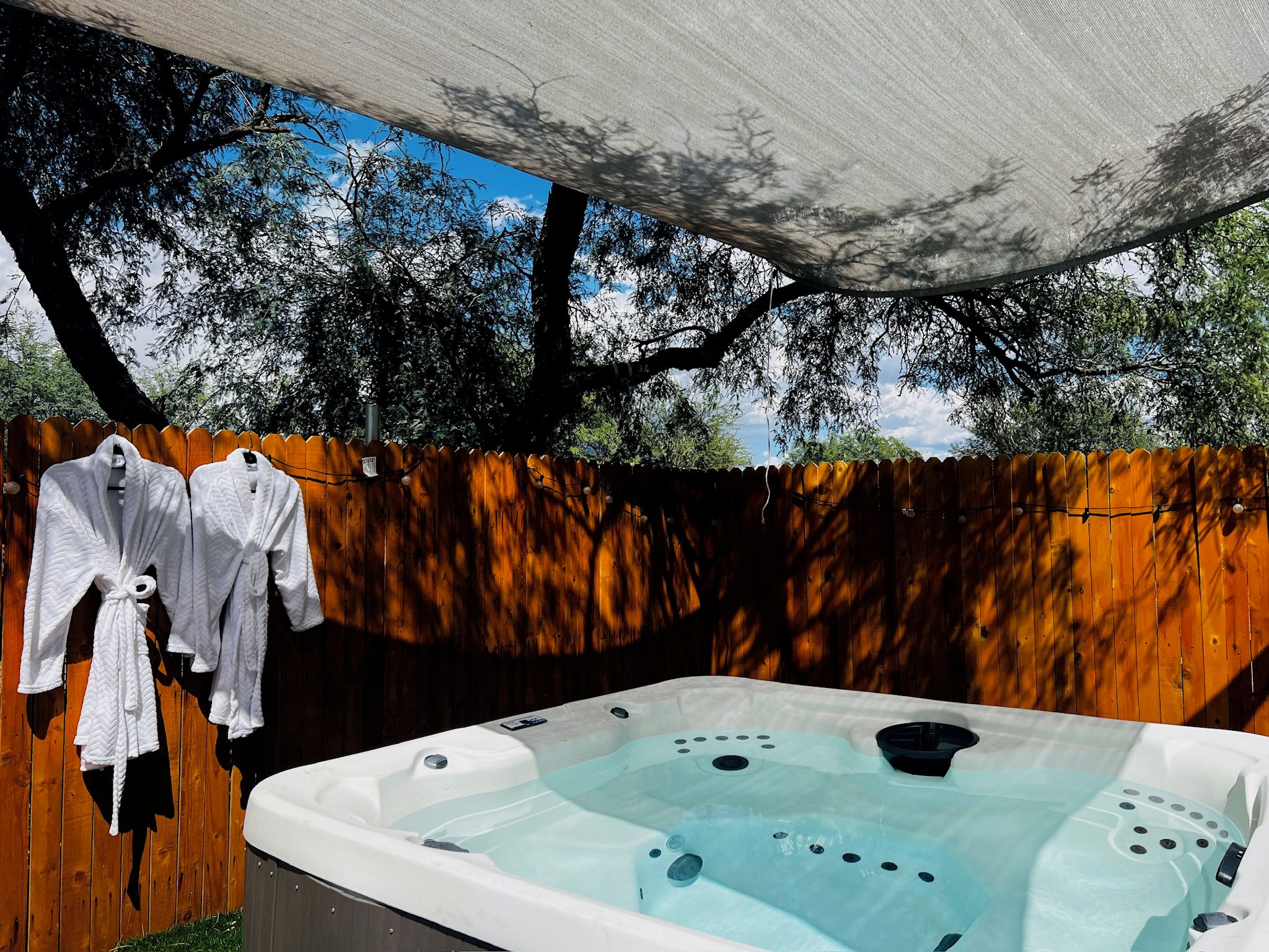 A hot tub under a canopy with a wooden fence and trees in the background.