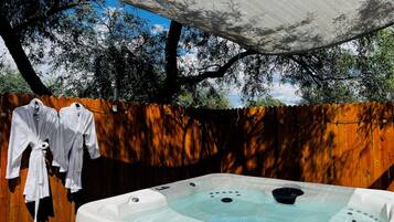 A hot tub under a canopy with a wooden fence and trees in the background.