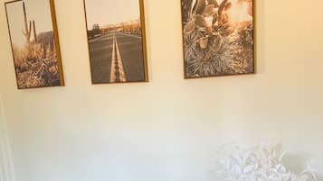 Ein Zimmer mit drei gerahmten Fotografien an der Wand, zwei grüne Sessel und eine künstliche Pflanze.