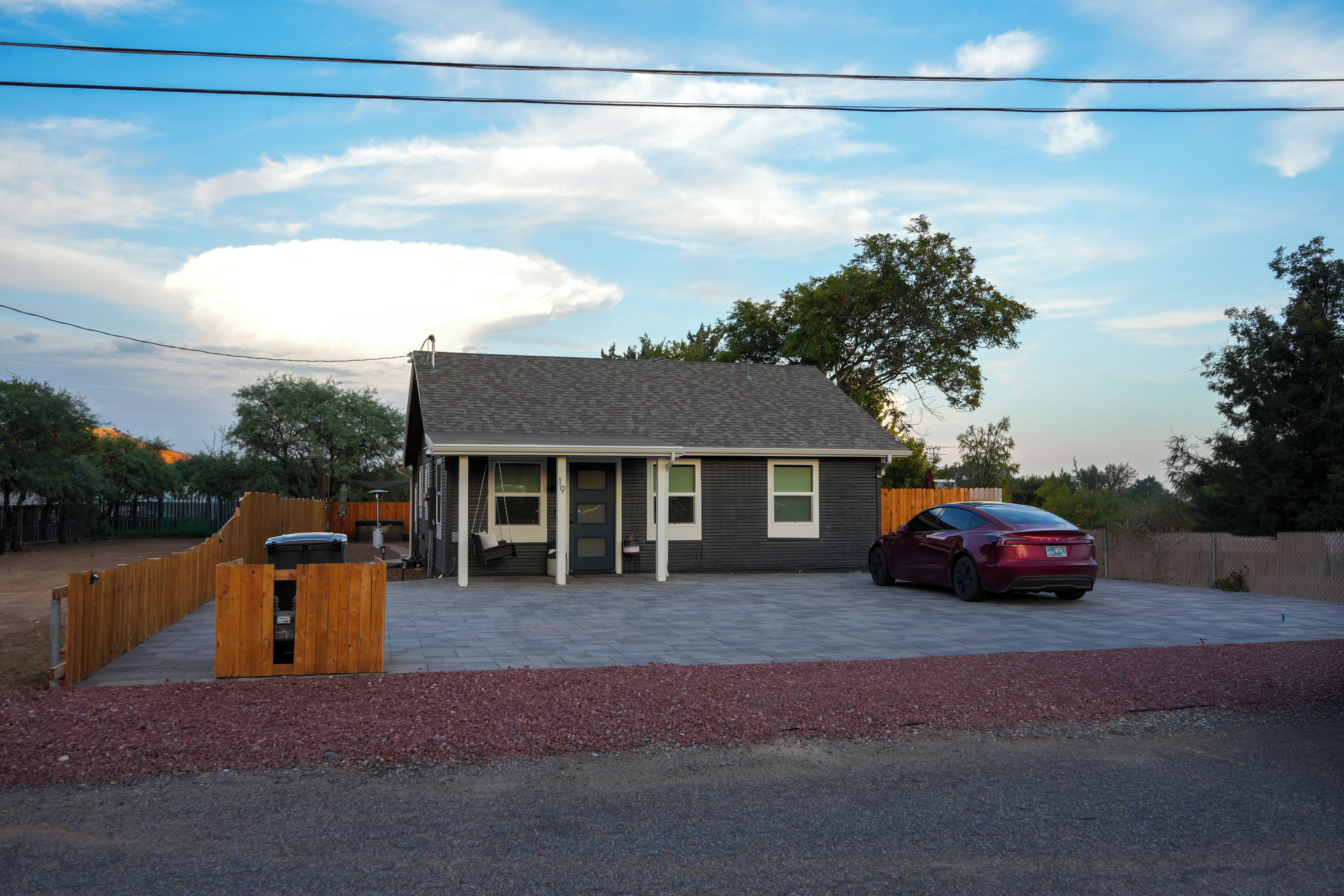A single-story house with a covered porch, a car parked in the driveway, and a fenced backyard.
