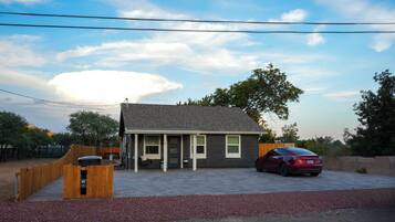 A single-story house with a covered porch, a car parked in the driveway, and a fenced backyard.