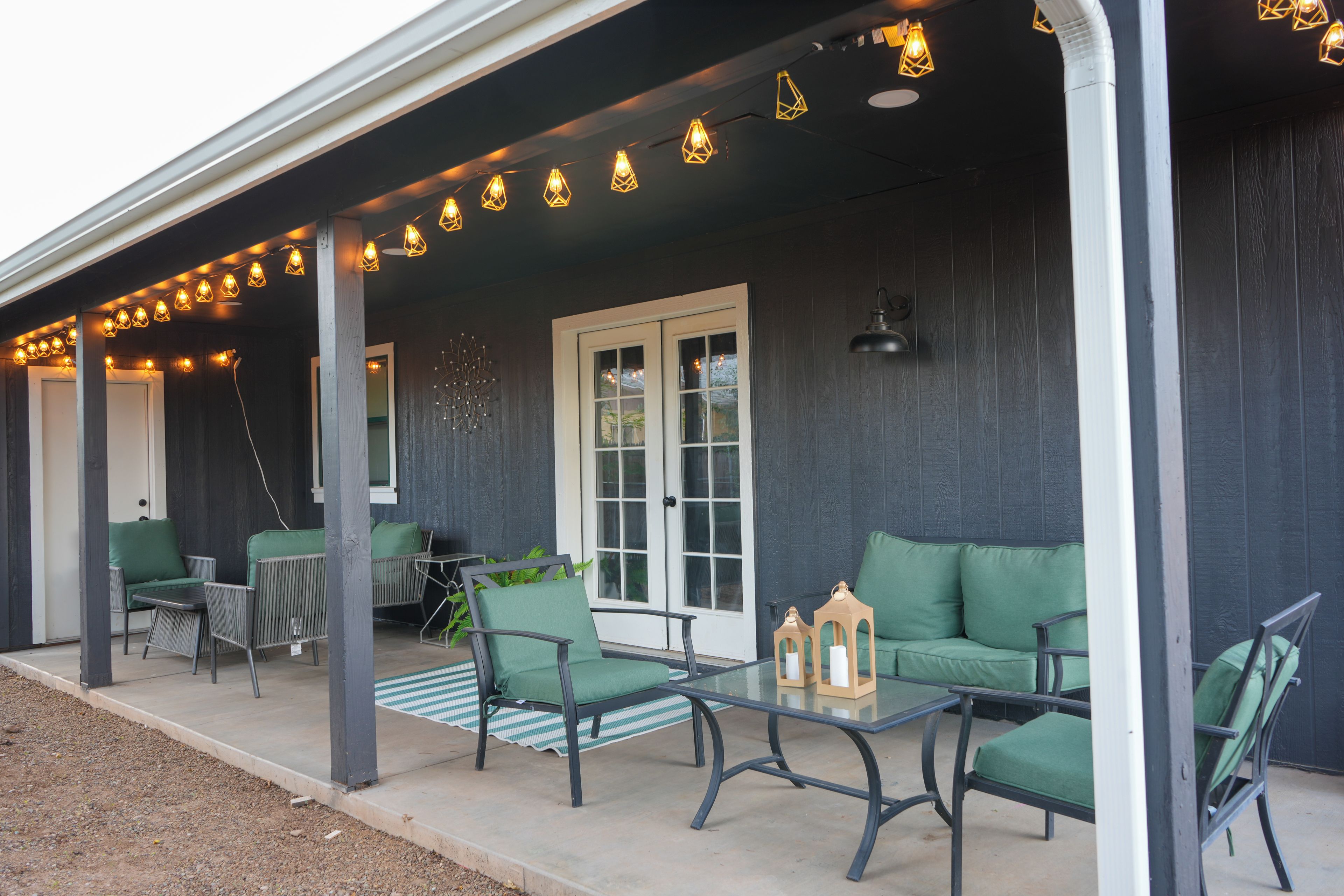 A covered porch with outdoor seating, string lights, and a window.