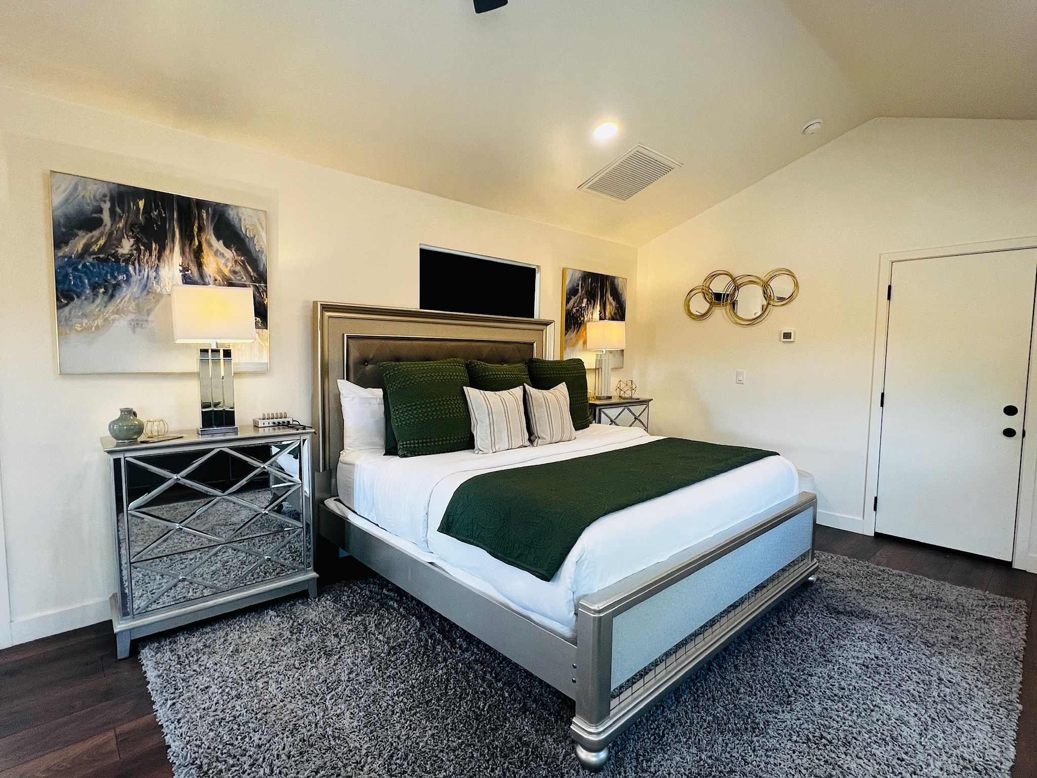 A hotel room with a bed, bedside tables, artwork on the walls, and a door.