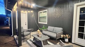 Espaço ao ar livre com assentos, incluindo sofá, cadeiras e mesa, com decoração na parede e luzes de cordão.