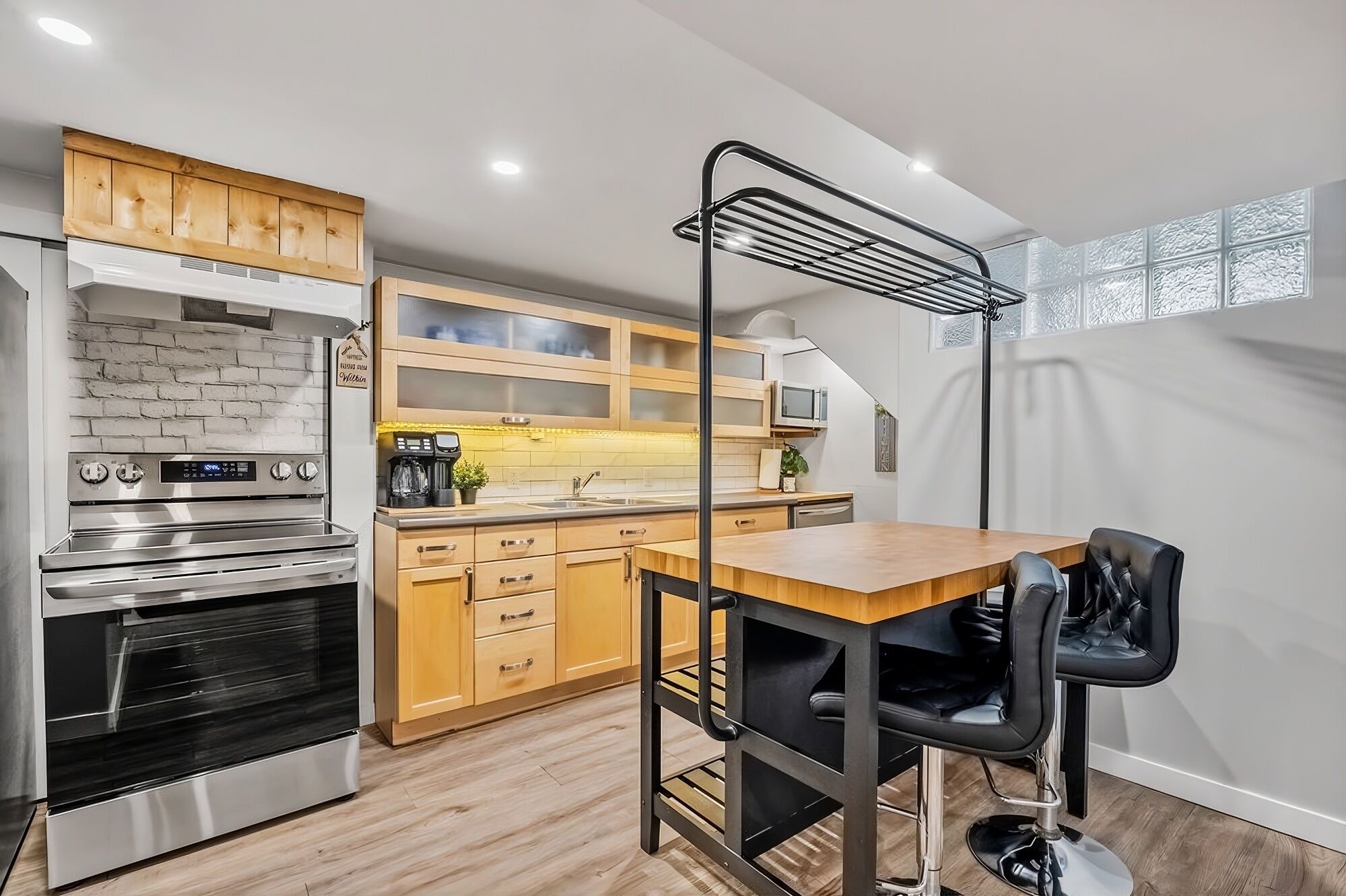 Une cuisine compacte avec des meubles en bois, un four en acier inoxydable, un micro-ondes et une chaise noire placée devant une table en bois.