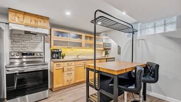 Une cuisine compacte avec des meubles en bois, un four en acier inoxydable, un micro-ondes et une chaise noire placée devant une table en bois.
