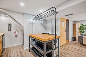 Una cocina moderna con una mesa de madera, un estante de metal negro y una escalera que conduce a otra habitación.