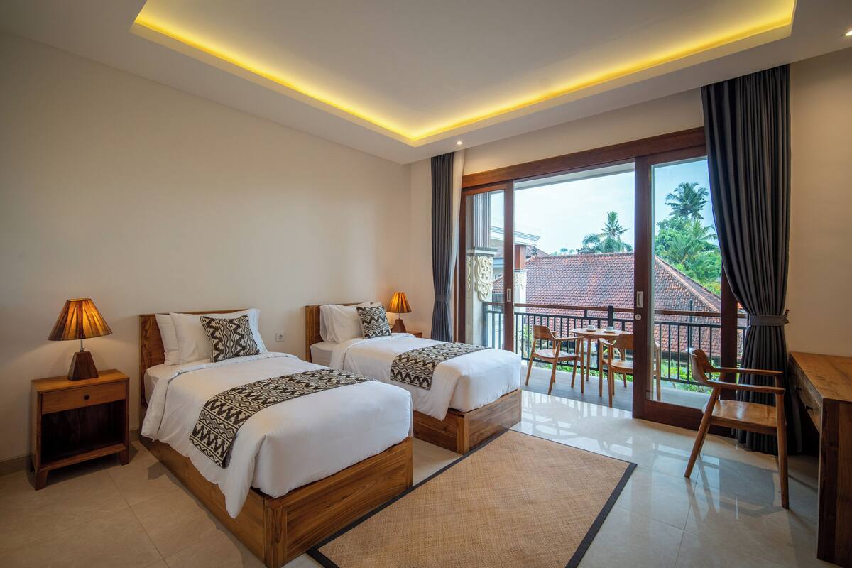 Een hotelkamer met twee bedden, een balkon met een tafel en stoelen en uitzicht op de omgeving.