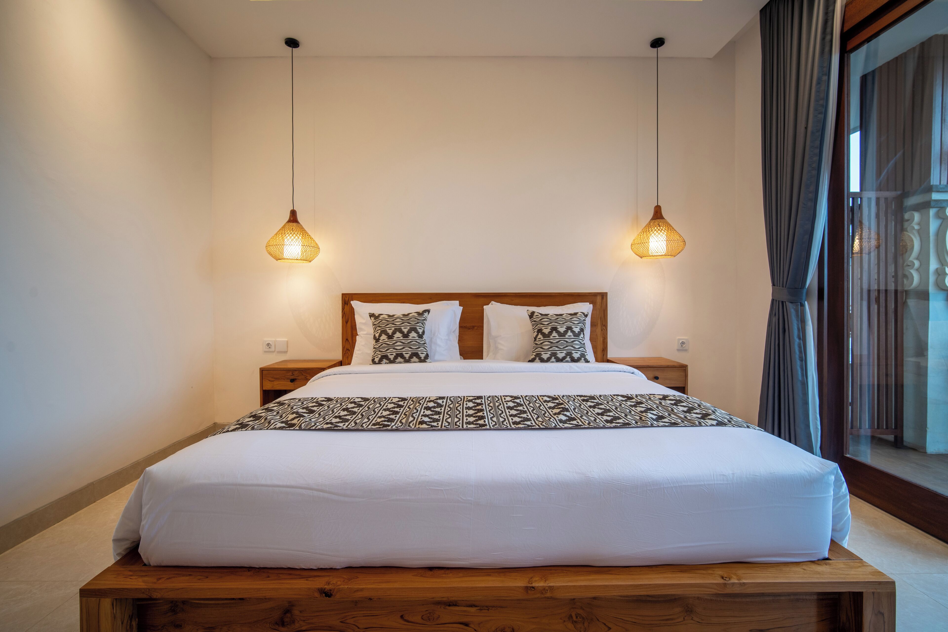 A neatly made bed with a wooden headboard, two bedside tables, and hanging pendant lights.