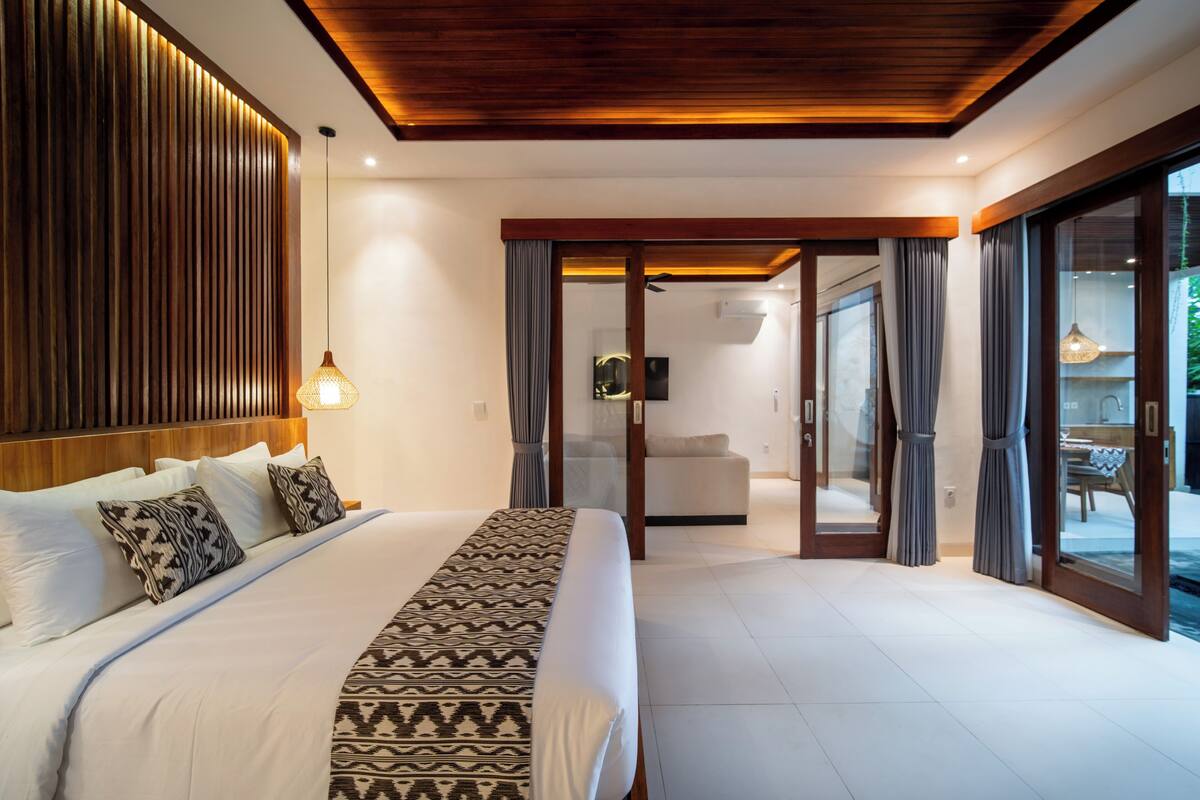 Een moderne slaapkamer met een groot bed, een houten plafond en een schuifdeur van glas die uitkomt op een balkon.