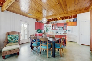 Ein Essbereich mit Holztisch und Stühlen, ein Korbstuhl mit Kissen und einem Deckenventilator.