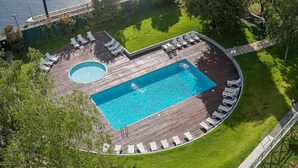 Oversigtsbillede af et poolområde med et rektangulært pool, et cirkulært boblebad, og flere liggestole placeret omkring poolen.