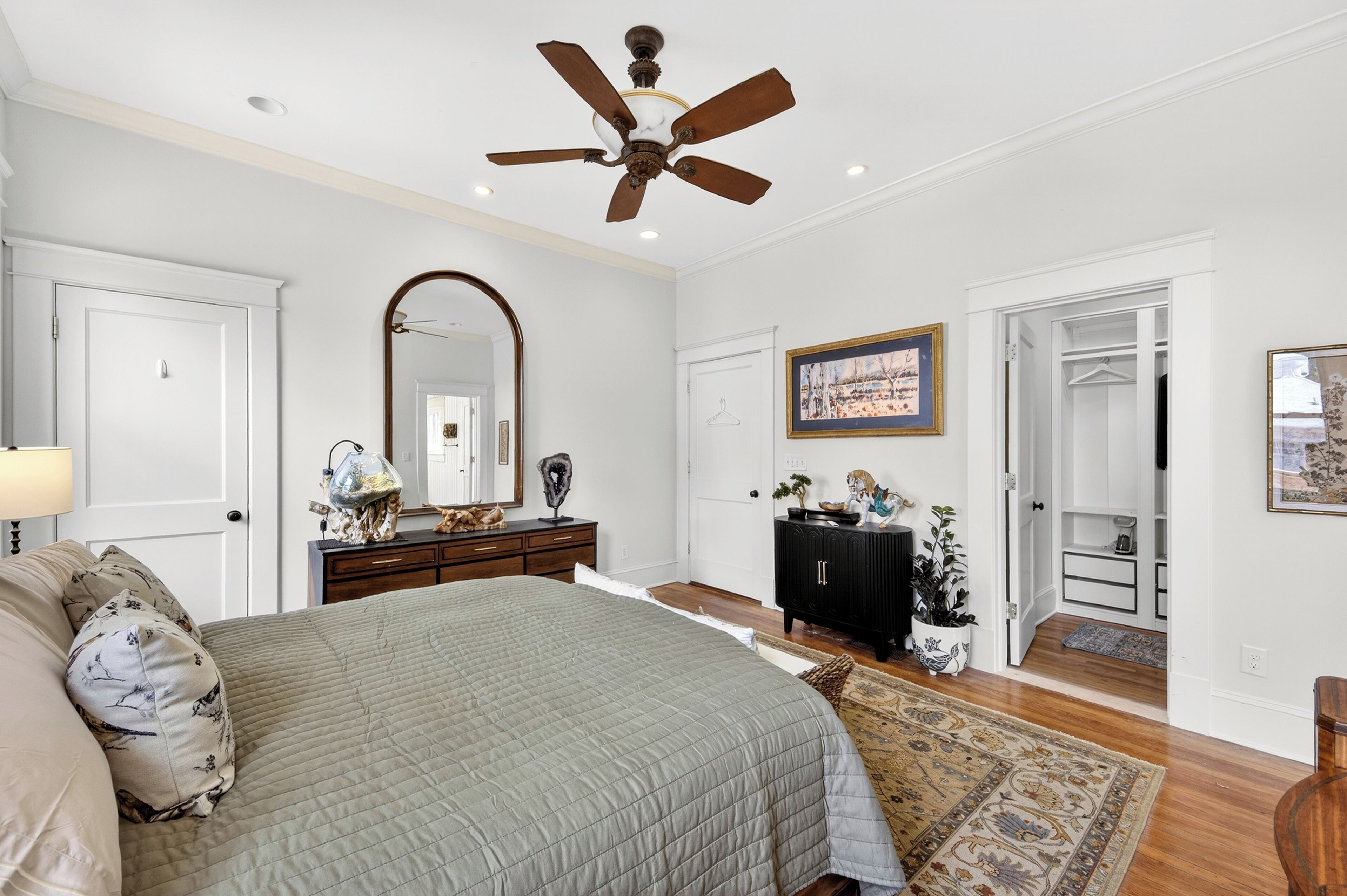 A bedroom with a large bed, a ceiling fan, a dresser, a mirror, and a wardrobe.