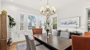 A dining area with a large wooden table, upholstered chairs, a chandelier, and a view of the outdoors through large windows. - Comfort and Space with convenience (Atlanta)