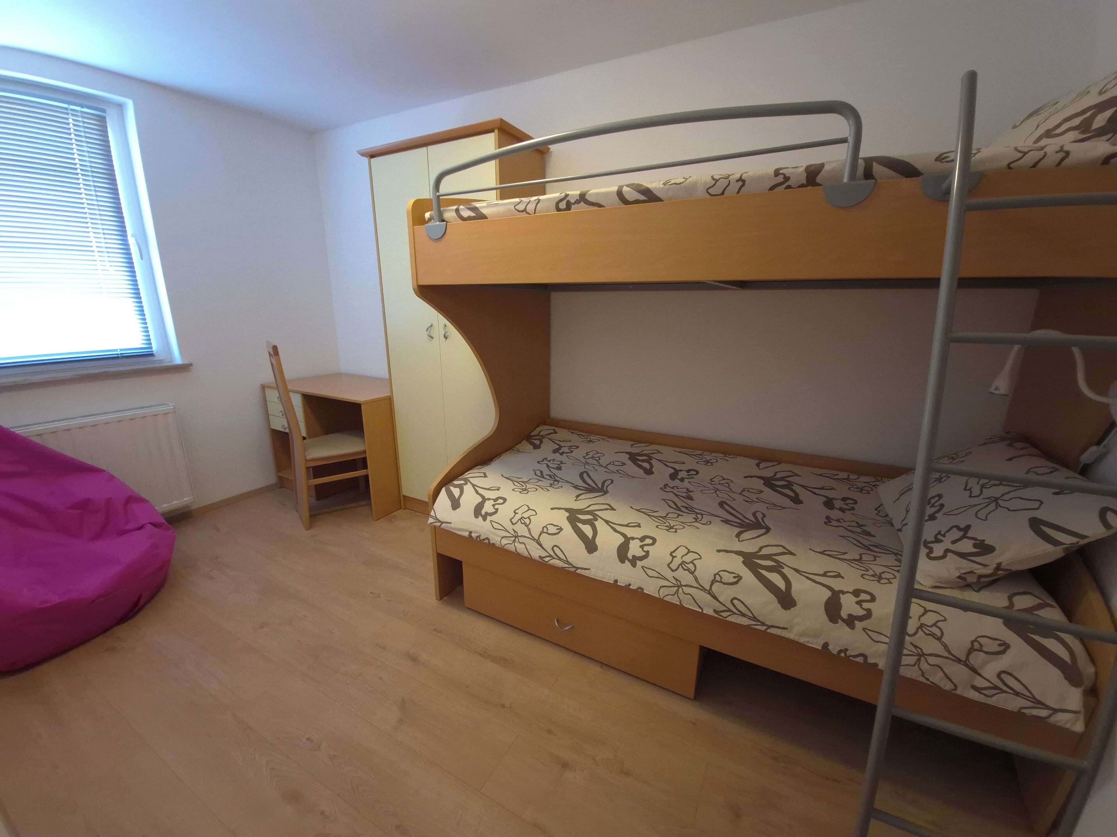 A bunk bed with a desk and chair, a radiator, and a window with blinds.