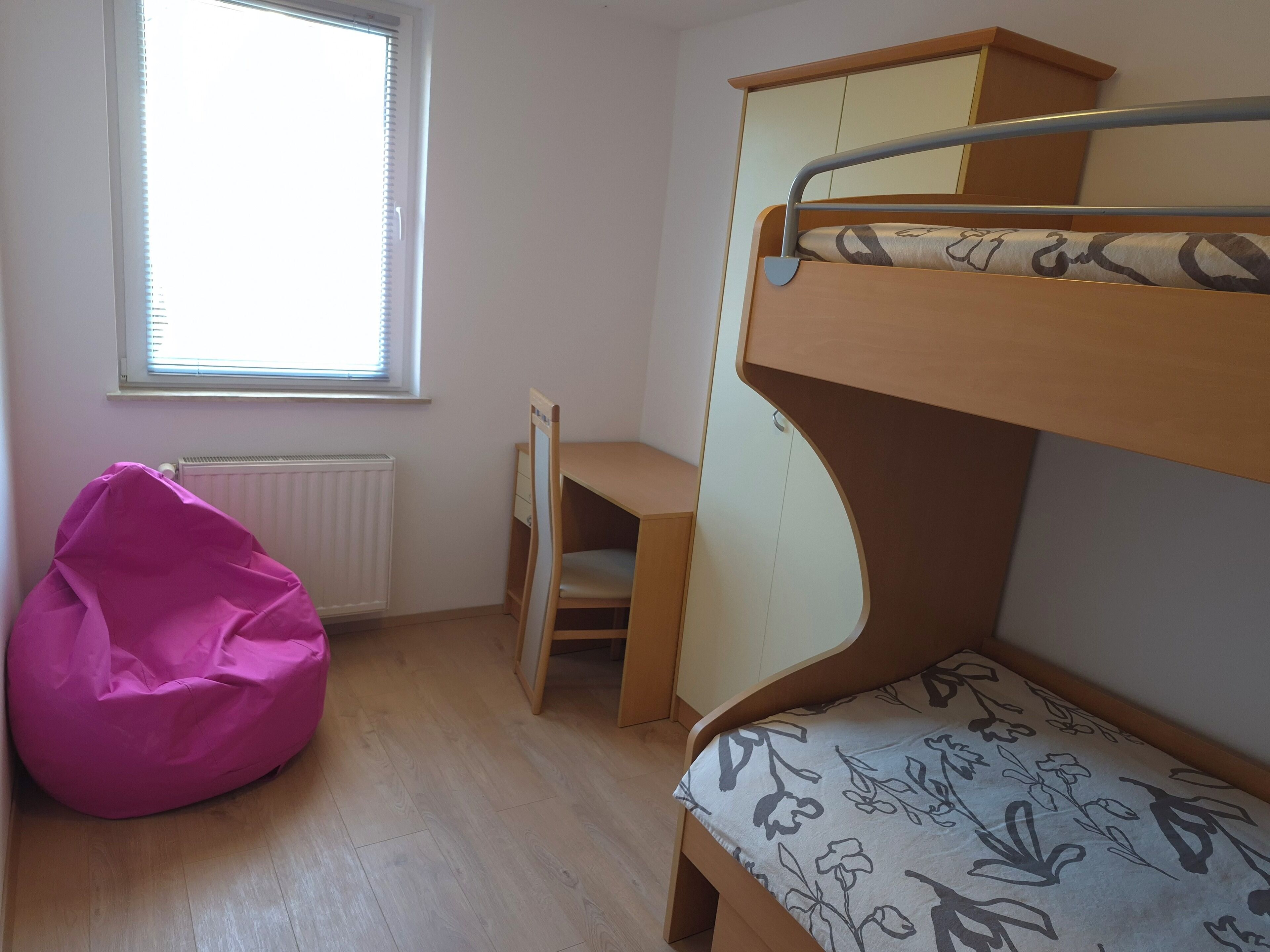 Una camera con letto a castello, termosifone e una poltrona sacco rosa.