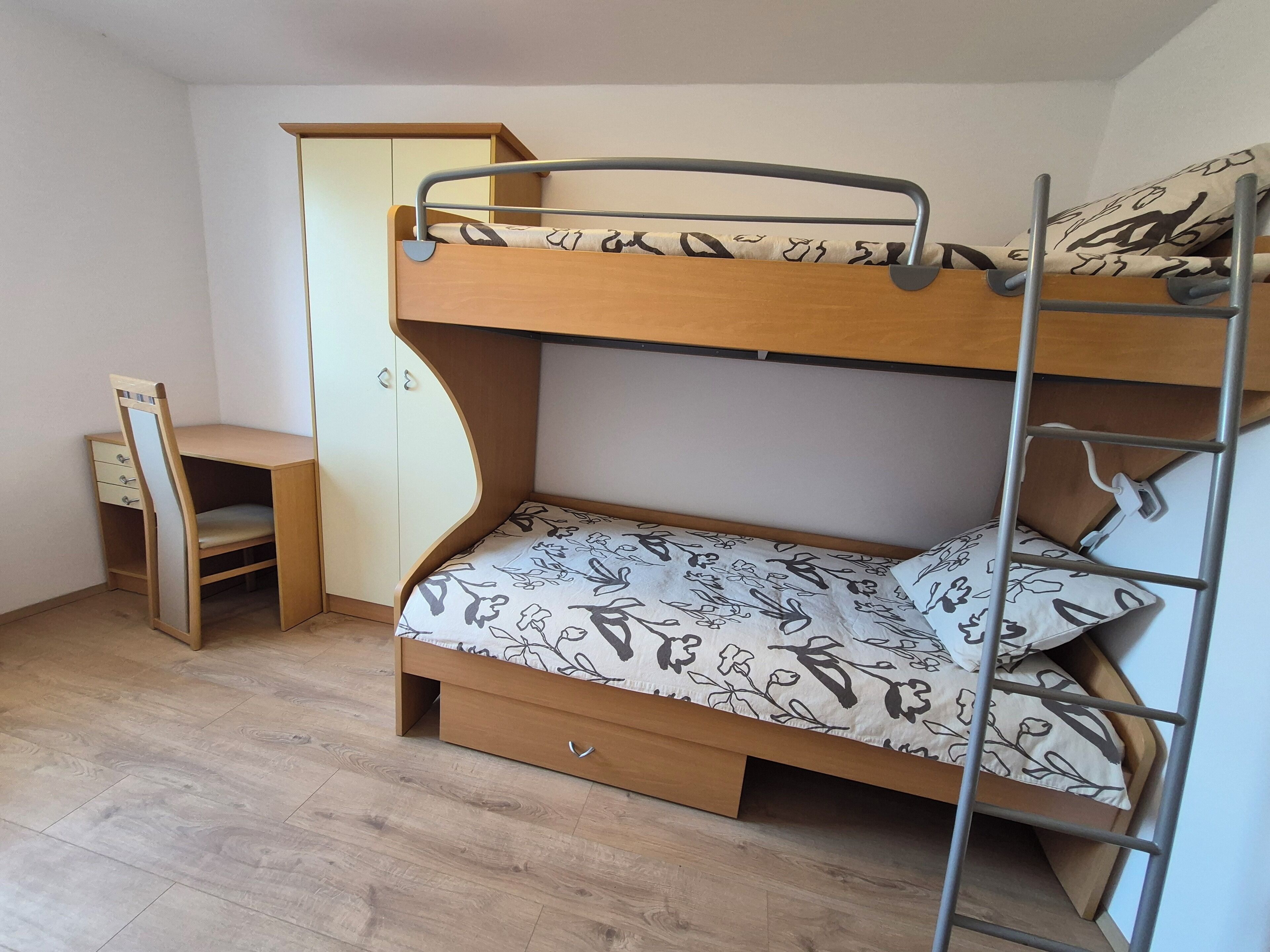 Un lit superposé avec un bureau et une armoire dans une pièce dont le sol est recouvert de parquet.
