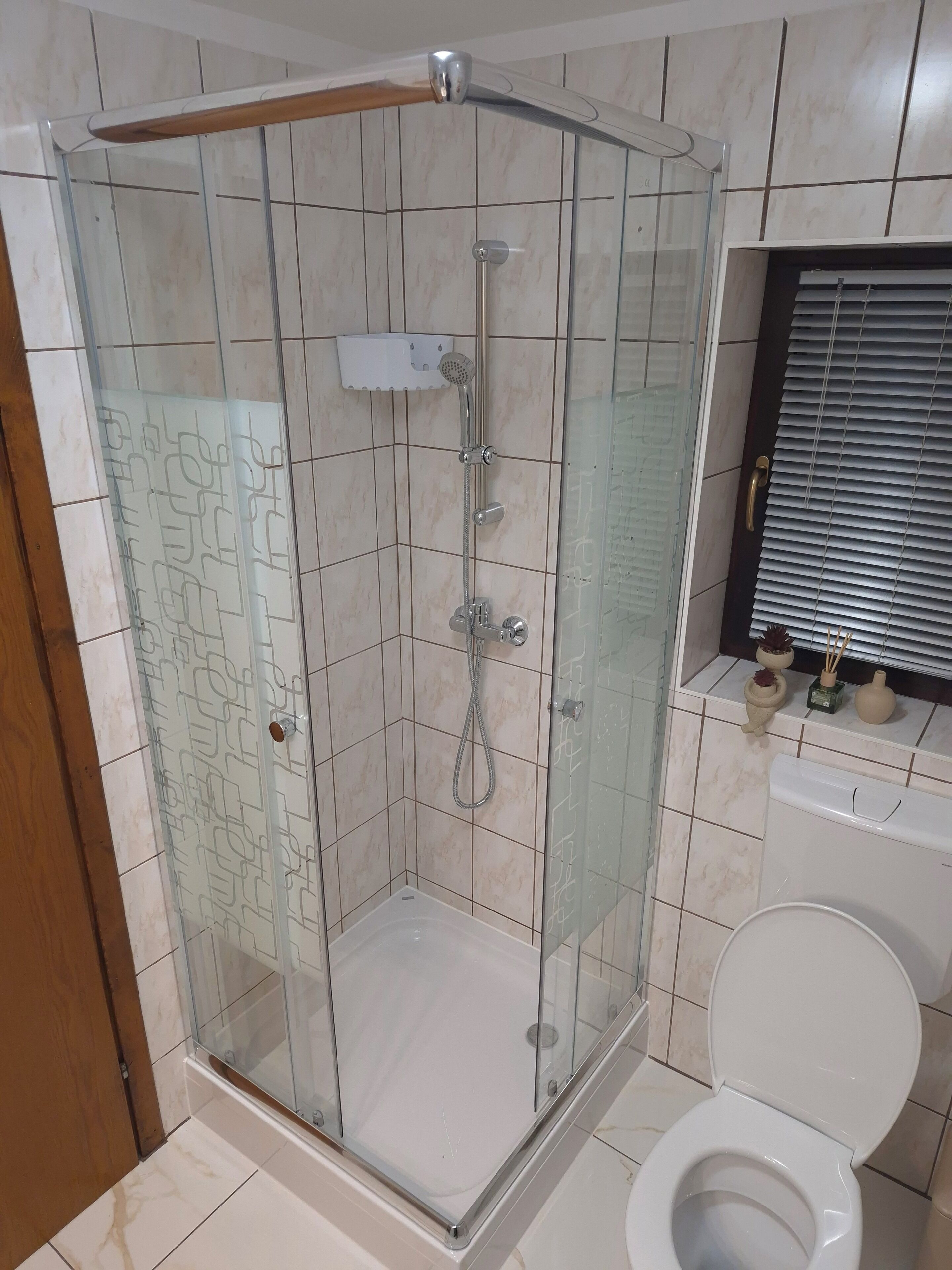 Une douche fermée par des parois en verre, dotée d’un pommeau de douche à main et d’un robinet mural.