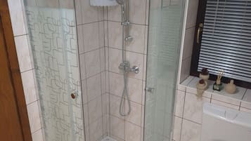 Une douche fermée par des parois en verre, dotée d’un pommeau de douche à main et d’un robinet mural.