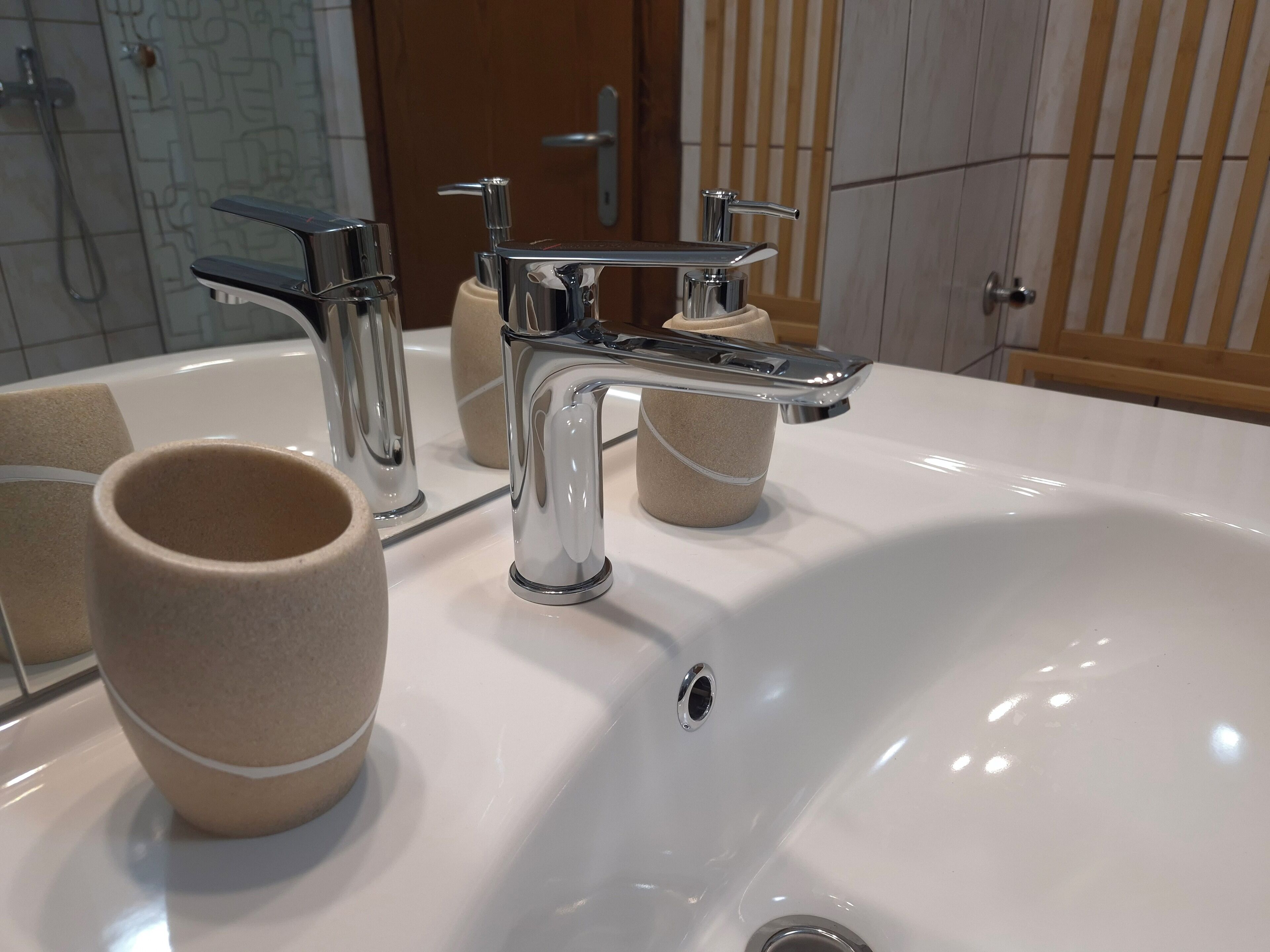 Un baño con un lavamanos blanco, grifos cromados y toallas color crema.