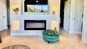 Un salón con una televisión de pantalla plana sobre la chimenea, flanqueado por apliques de pared.