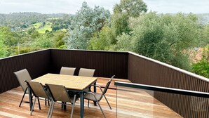 Una terraza con una mesa y sillas, con vistas a un paisaje verde con árboles y colinas.