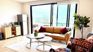 Una sala moderna con un sofá, un sillón estampado, una mesita redonda pequeña, un aparador y un ventanal con vistas.