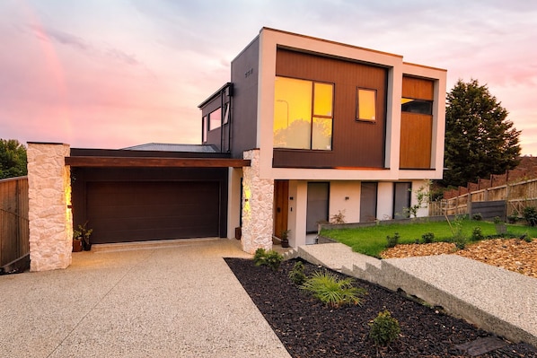 Ein modernes, zweistöckiges Haus mit Garage, Steinpfeilern und einem angelegten Garten.