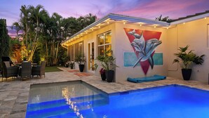 Ein modernes Haus mit Swimmingpool, einer Terrasse mit Gartenmöbeln und einem Wandgemälde von Delfinen an der Außenwand.