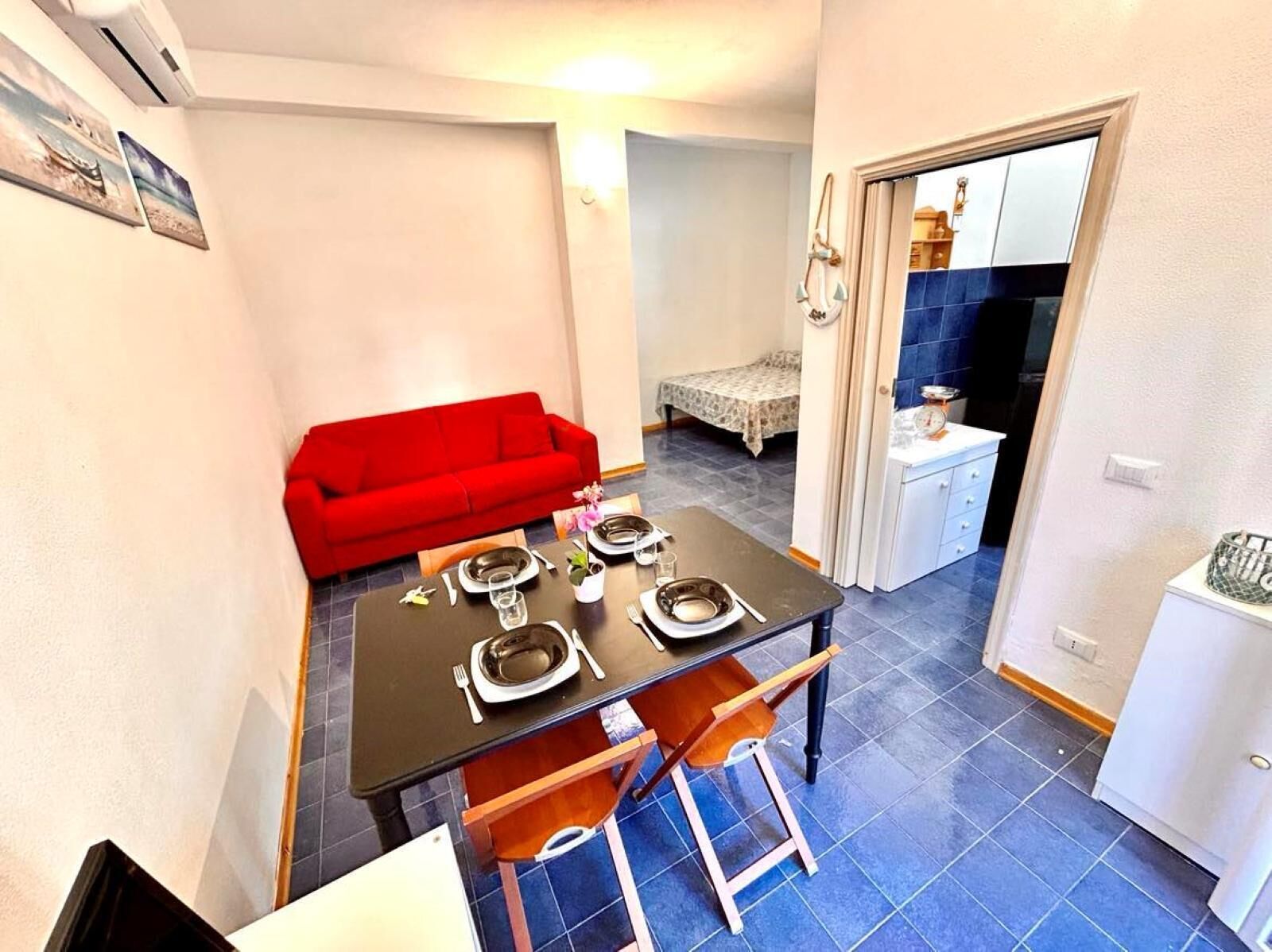 A compact living space with a dining area, a red sofa, a small kitchenette, and a bathroom visible through an open door.