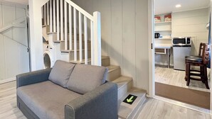Ein modernes Wohnzimmer mit einem grauen Sofa, einer Treppe und einem durch eine offene Tür einsehbarer Küchenbereich.