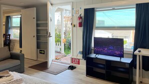 Ein Wohnzimmer mit einer Couch, einem Fernseher auf einem Schrank, einer Tür, die nach draußen führt, und einem Feuerlöscher an der Wand.