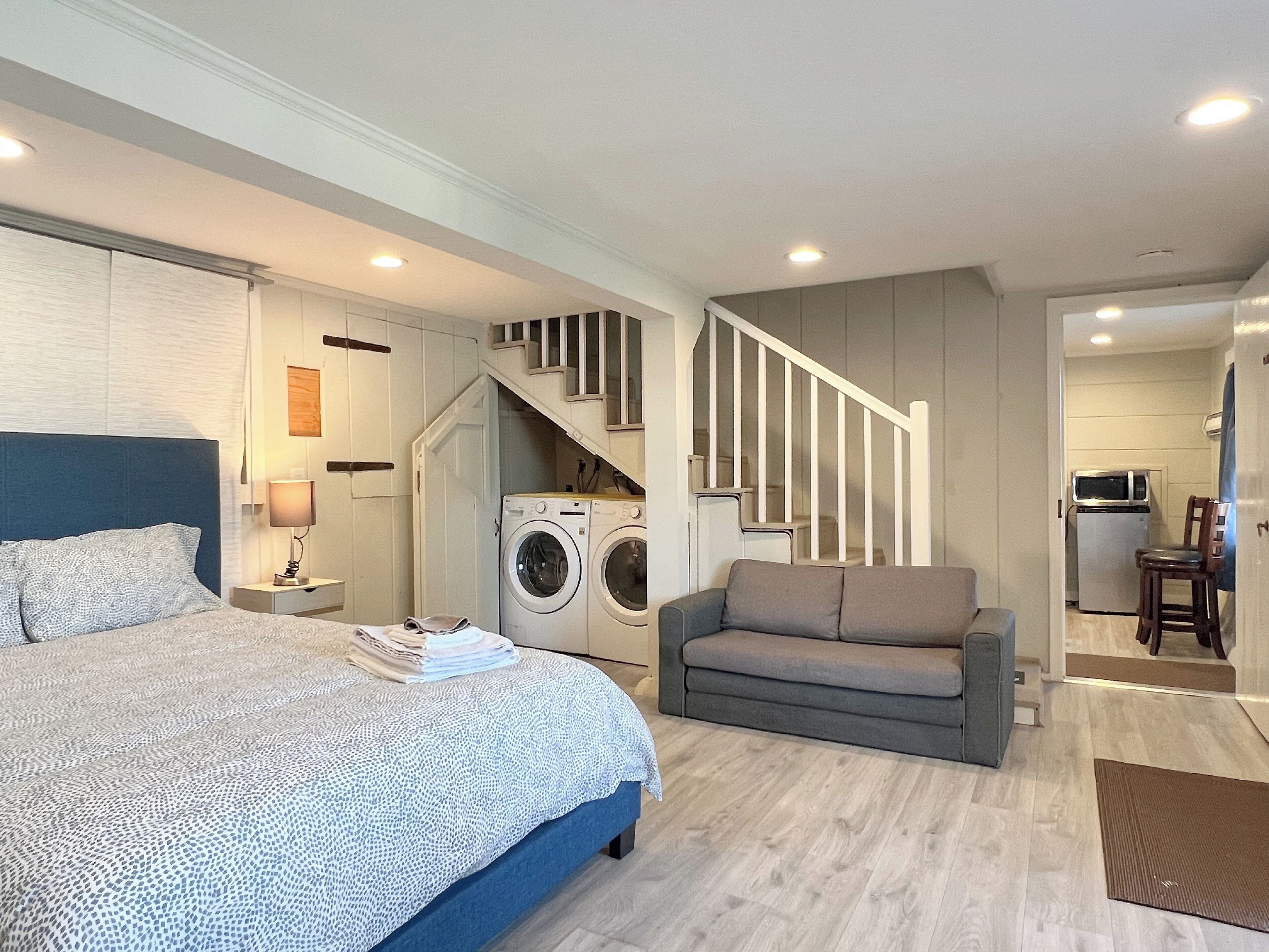Quarto com cama, máquina de lavar, sofá e escada que dá para uma cozinha.