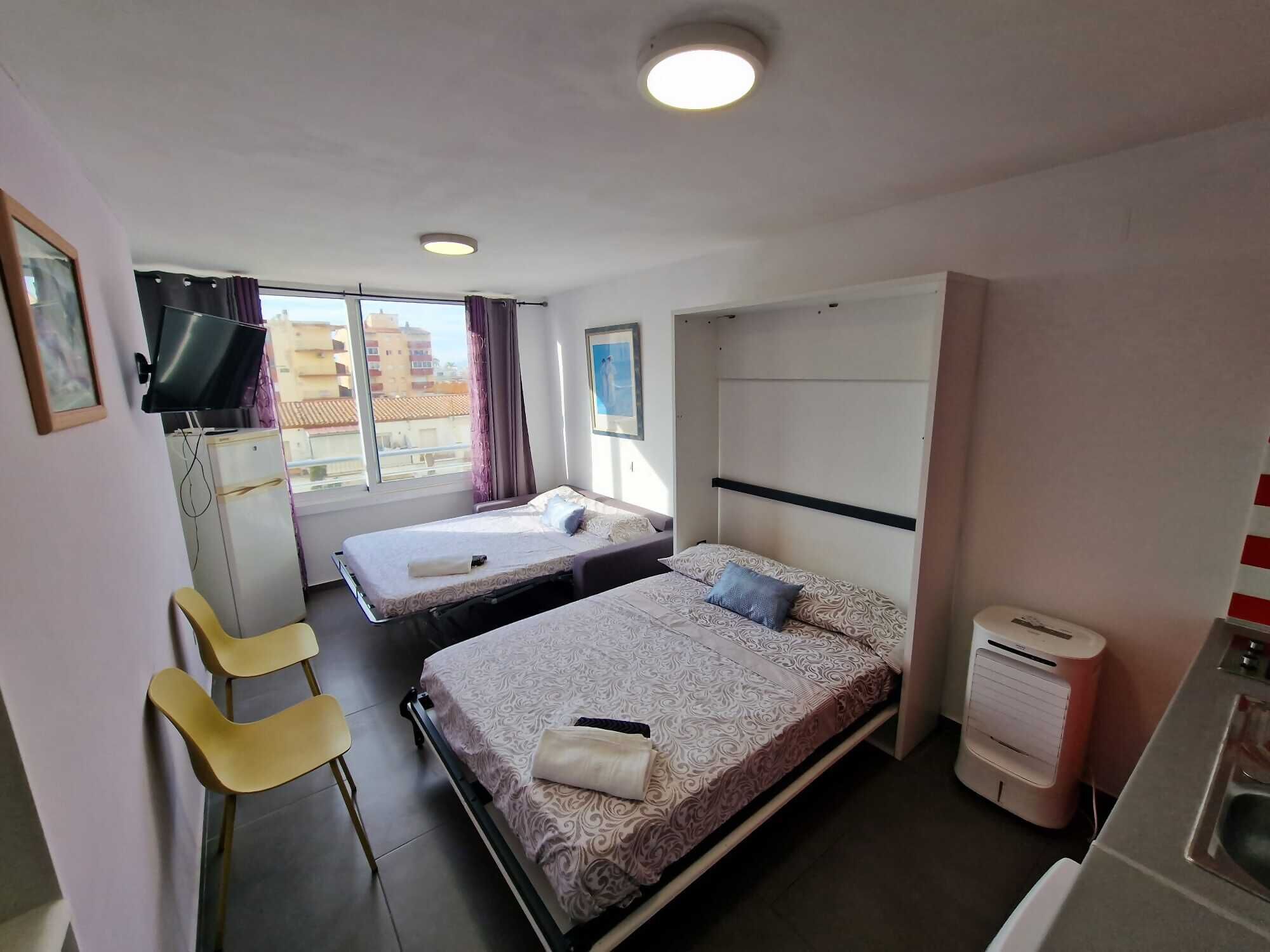 Una habitación de hotel pequeña con dos camas, un escritorio, una silla y una kitchenette.