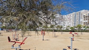 Un espace de remise en forme en plein air, équipé de matériel d’exercice, entouré d’arbres et avec un bâtiment en arrière-plan.
