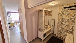Une petite pièce comprenant un lit superposé, un petit bureau avec une chaise et, au fond, un coin cuisine.