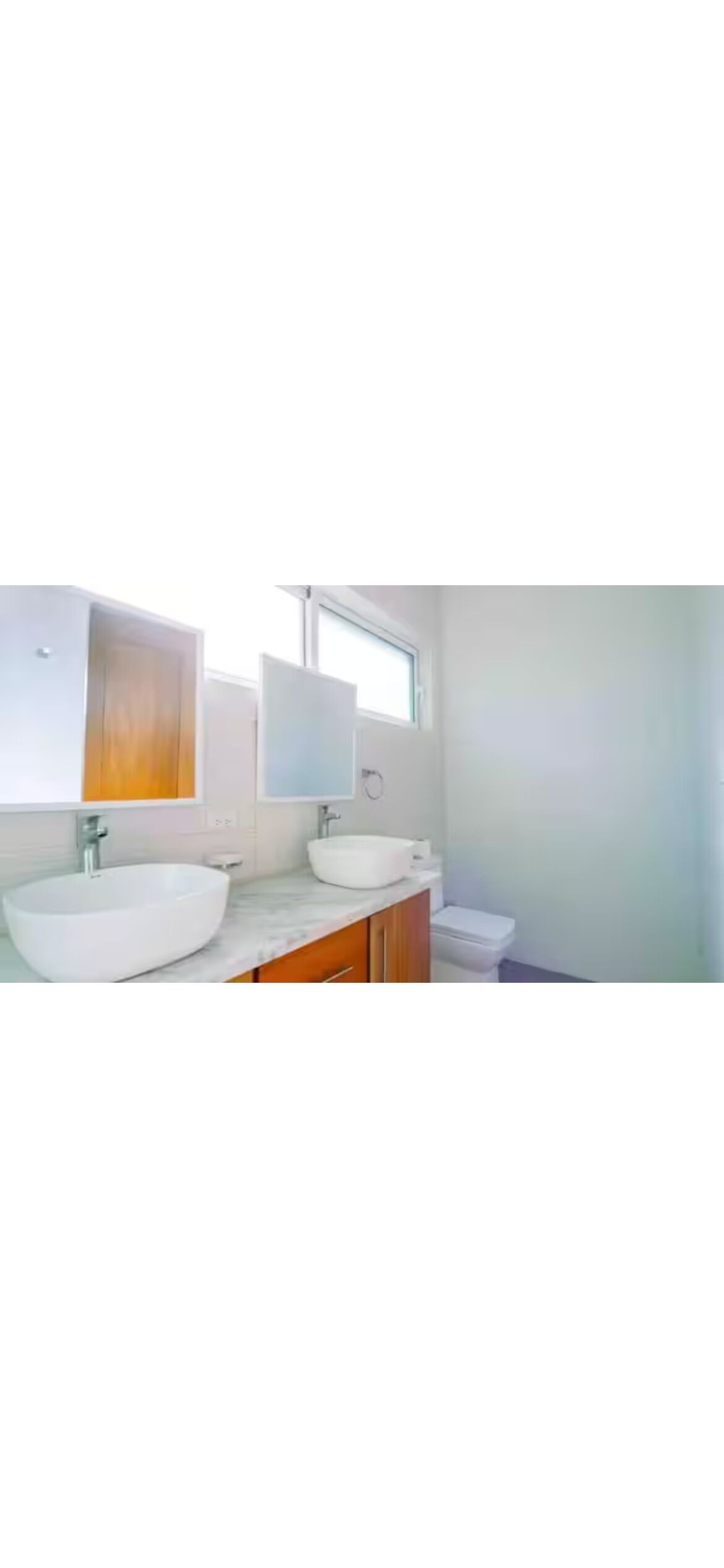 Un baño moderno con dos lavamanos tipo recipiente blancos, armarios de madera y un espejo grande.