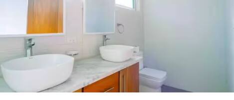 A modern bathroom with two white vessel sinks, wooden cabinets, and a large mirror.
