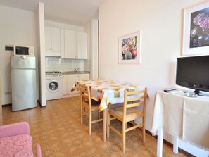 A compact living space with a kitchenette, a dining area with a table and chairs, a television, and a washing machine. - Cosy apartment for 4 people with A/C, WIFI, TV, balcony and pets allowed (San Michele Al Tagliamento)