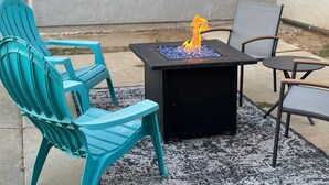 Un espace patio comprenant une table carrée, deux chaises et un petit foyer.