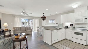 A modern living room with a sofa, coffee table, and a dining area. The kitchen features white cabinets, a microwave, and a dishwasher. - Easy Coastal Living Meets Relaxed Island Comfort | Heated Pool Access (Tybee Island)