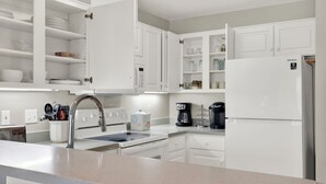Une cuisine moderne avec des meubles blancs, un évier en acier inoxydable, un four encastré, un réfrigérateur et une machine à café.