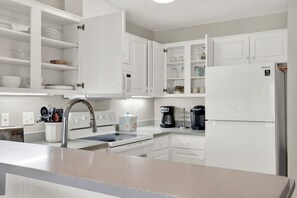 A modern kitchen with white cabinetry, a stainless steel sink, a built-in oven, a refrigerator, and a coffee maker. - Easy Coastal Living Meets Relaxed Island Comfort | Heated Pool Access (Tybee Island)