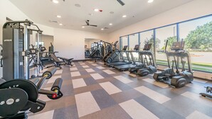 Een sportschool met trainingsapparatuur, een plafondventilator en grote ramen.