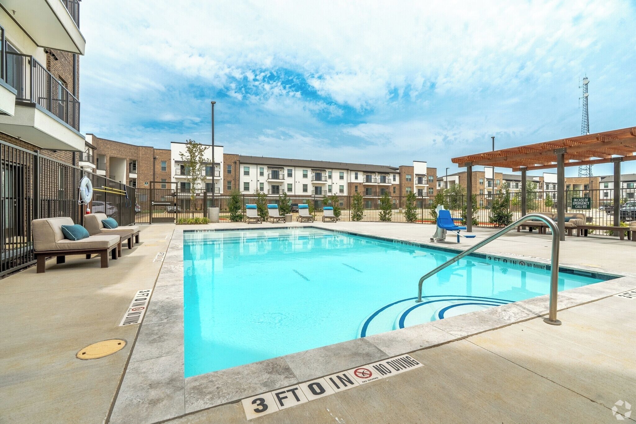 A swimming pool with lounge chairs, a pergola, and a building with multiple floors in the background.