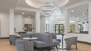 Een moderne lounge met grijs gestoffeerde zitting, een centraal hanglamp en uitzicht buiten door grote ramen.